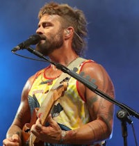 a man with a beard and tattoos singing into a microphone