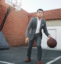 a man in a suit holding a basketball in front of a basketball hoop